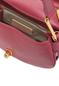 Borsa a tracolla in pelle rosa con hardware dorato, dotata di un compartimento con zip e di un'etichetta interna. Forma arrotondata con chiusura a patta.