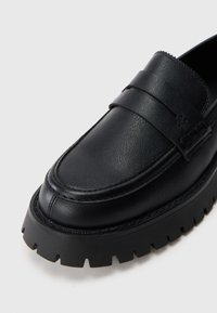 Černé kožené mokasíny s kulatou špičkou, zvýšeným prošíváním a silnou, vroubkovanou gumovou podrážkou pro lepší trakci.