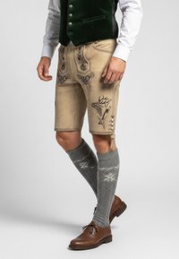 Beige lederhosen met geborduurde herten en bloemmotieven, gecombineerd met grijze kniekousen met witte patronen en bruine leren schoenen.