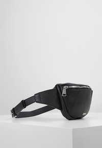 Marsupio in pelle nera con finitura texture, chiusura a zip e tracolla regolabile. Presenta dettagli in metallo argentato e un design compatto.