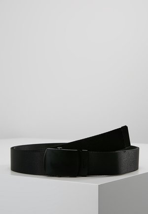 Ceinture en tissu noir avec une boucle rectangulaire noire mate et lisse posée sur une surface blanche sur fond uni.