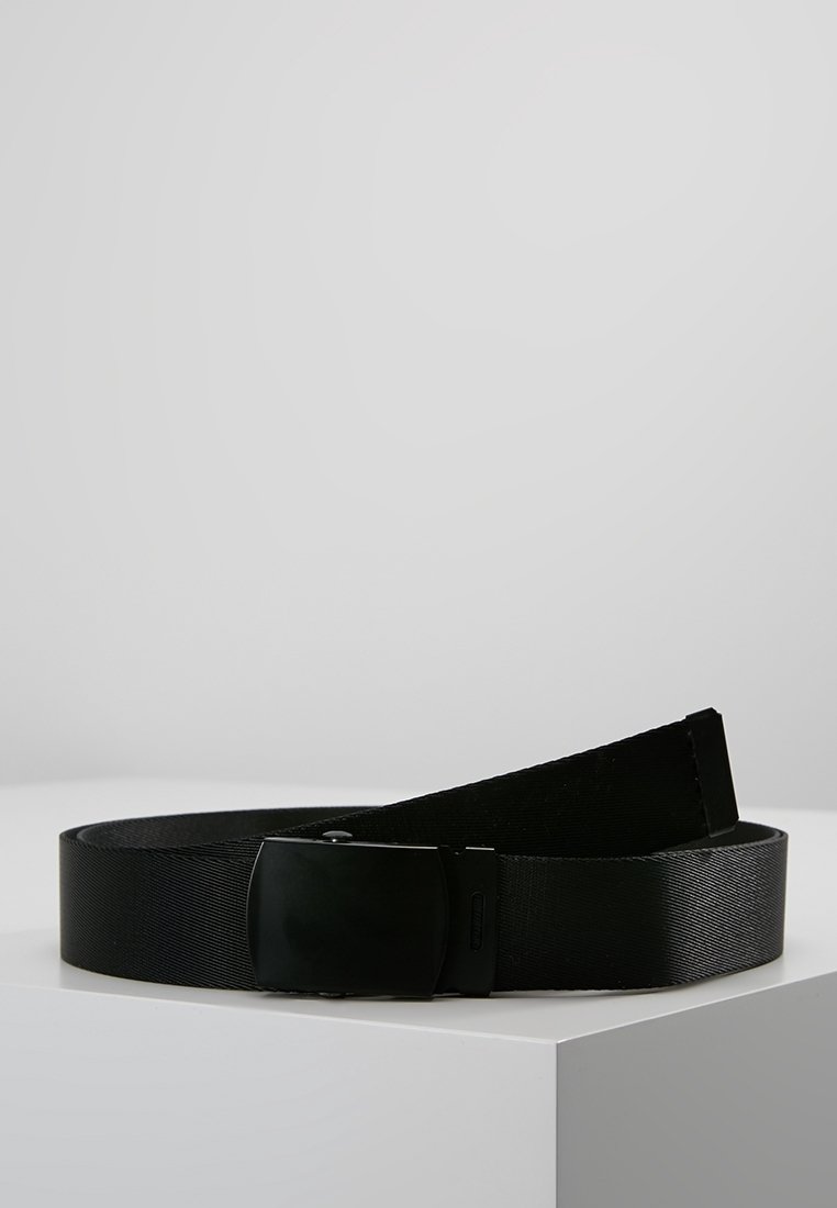 Ceinture en tissu noir avec une boucle rectangulaire noire mate et lisse posée sur une surface blanche sur fond uni.