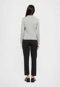 Polo gris à manches longues avec un col, associé à un jean noir à coupe droite et des chaussures noires, vu de derrière.