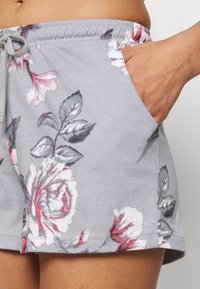 Shorts gris à motifs floraux avec une ceinture à cordon, ornés de motifs de roses roses et blanches, et poches latérales pour plus de praticité. Texture douce.