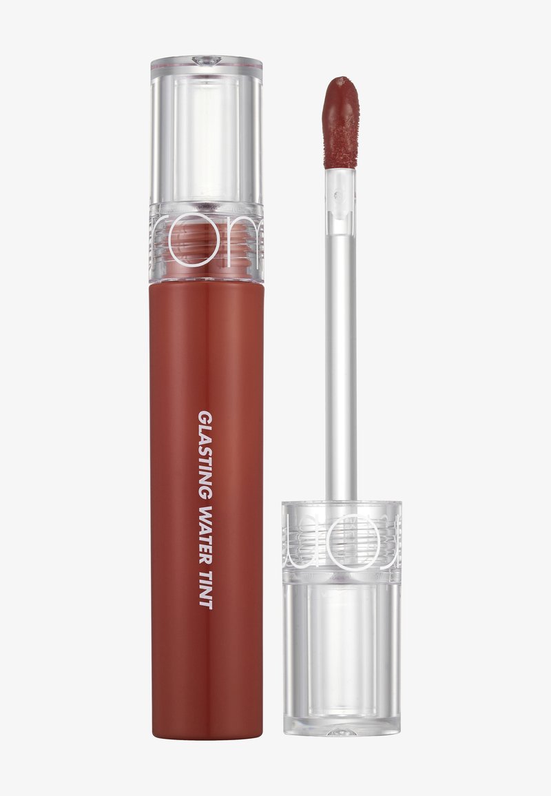 Balsam do ust w przezroczystej tubce z brązowym odcieniem. Posiada aplikator w kształcie stopy jelenia oraz etykiety z napisem "Glasting Water Tint" na białym tle.