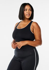 Reggiseno sportivo nero con accenti bianchi, caratterizzato da una scollatura a barco e spalline larghe, abbinato a leggings neri con una striscia bianca laterale.