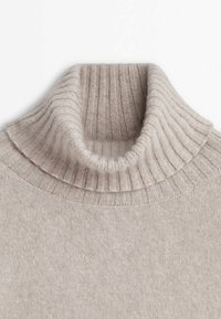 Beige ribbad polokrage med en mjuk textur. Kragen har en dubbellagerdesign som kompletterar kroppens släta stickning.