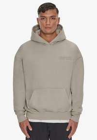 Sweat-shirt à capuche gris avec une poche avant, épaules tombantes, poignets côtelés et logo "DROPSIZE" dans une teinte plus claire.