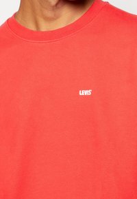 Rotes kurzärmliges Baumwoll-T-Shirt mit Rundhalsausschnitt und einem weißen "LEVI'S"-Logo auf der Brust, mit einer glatten Textur.