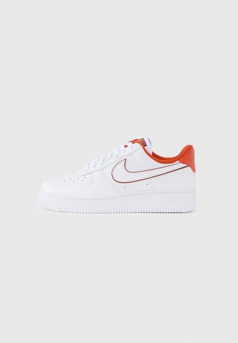 Fehér bőrből készült sportcipő narancssárga részletekkel, texturált gumitalppal, lyukasztott mintával a lábujjrészén, valamint a klasszikus vörös Nike Swoosh logóval.