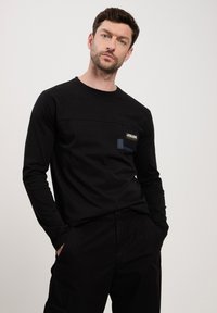 Czarna koszula z długim rękawem z kieszonką, z logo i kontrastowymi akcentami materiałowymi. Wykonana z miękkiego materiału, o luźnym kroju.