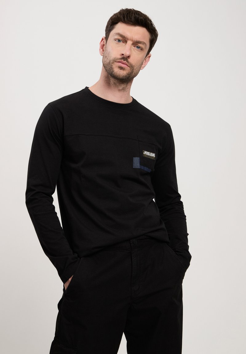 Czarna koszula z długim rękawem z kieszonką, z logo i kontrastowymi akcentami materiałowymi. Wykonana z miękkiego materiału, o luźnym kroju.