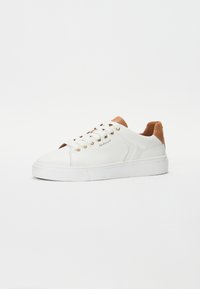 White leather sneaker with a tan suede heel and gold eyelets. Features visible stitching and a textured rubber sole for traction.
