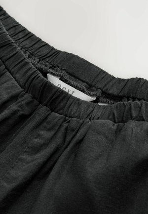 Fascia elastica nera con texture arricciata, dotata di un'etichetta di tessuto cucita all'interno. Il tessuto appare morbido e leggero.