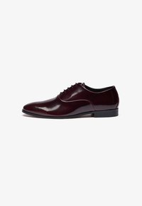 Chaussure de ville en cuir bordeaux avec finition polie, système de laçage, silhouette élégante et petit talon noir.