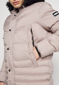 Puchowa kurtka w jasnym pastelowym różu z czarnymi akcentami, z kapturem wyłożonym sztucznym futrem, zapinanymi na zamek kieszeniami i haftowanym logo.