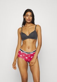 Zwarte gewatteerde bh en rode boyshorts met witte hartpatronen. De bh heeft dunne bandjes; de shorts hebben een zwarte elastische tailleband met het "ONLY" logo.