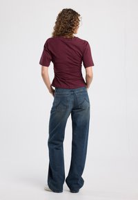Burgundy fitted top with short sleeves and gathered detail at the back, paired with high-waisted, wide-leg blue jeans.