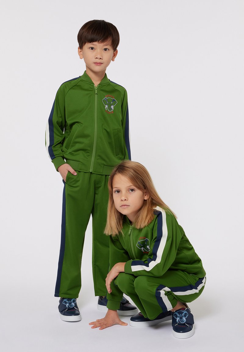 Tute da ginnastica verdi con accenti blu navy. Giacca con zip e pantaloni presentano un logo di elefante giocoso. Tessuto morbido e liscio con design sportivo.