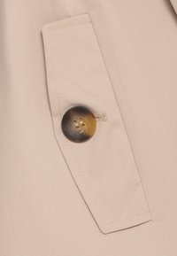 Beige szövet átlós szövésű, átlós zsebbel és négylyukú, foltos, kerek gombbal.