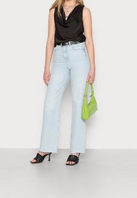 Top in satin nero con scollo a cowl, jeans a vita alta azzurri chiari a gamba larga, sandali neri con tacco intrecciato e borsa verde lime.