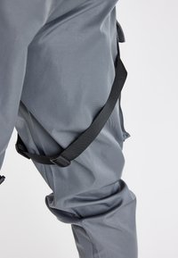 Harmaat vedenpitävät housut, joissa on sileä pinta, säädettävä musta hihna ja rento istuvuus lahkeissa.