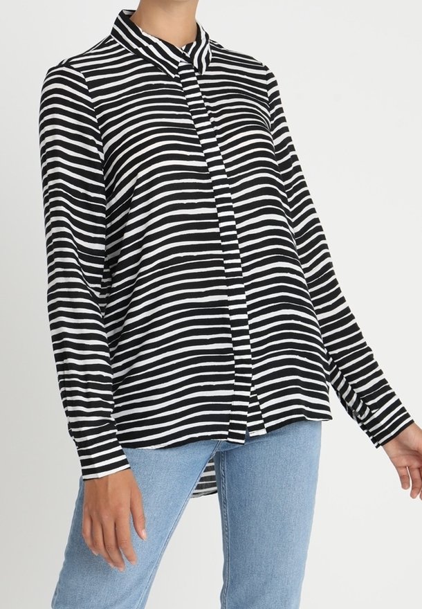 Femme portant un t-shirt à manches longues rayé horizontal noir et blanc associé à un jean bleu clair sur un fond uni.