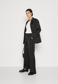 Black tailored suit with wide-leg trousers and a fitted blazer, accompanied by a white top and black loafers. Textured handbag is included.
