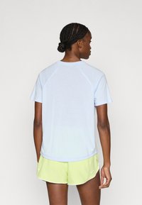 Αθλητική μπλούζα σε ανοιχτό γαλάζιο χρώμα με κοντά μανίκια και στρογγυλή λαιμόκοψη, συνδυασμένη με σορτς σε λάιμ πράσινο. Διαθέτει μανίκια ράγκλαν και απαλό ύφασμα.