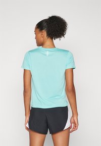 Turquoise sporttop met korte mouwen en een ronde halslijn, voorzien van een reflecterende streep aan de achterkant, gecombineerd met zwarte shorts met witte accenten.
