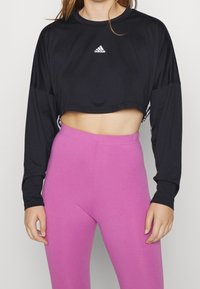 Czarny krótki, długi rękaw z logo Adidas, w połączeniu z różowymi legginsami z wysokim stanem, gładki materiał i dopasowany krój.