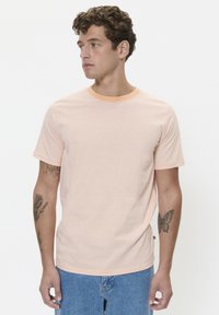 Striped short-sleeve t-shirt with an orange and white pattern, round neckline, and soft texture. Worn with light blue denim shorts.