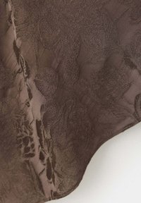 Tissu marron avec motif jacquard floral en relief et zones lisses, montrant la texture et les formes des fleurs en gros plan.