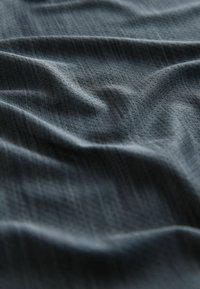 Material texturat într-o nuanță de gri cărbune profund, cu unduiții subtile și o țesătură fină, cu motive, care reflectă lumina în accente blânde.