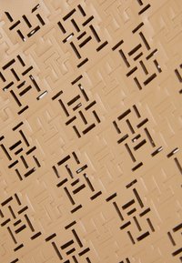 Béžový kožený povrch s intricátne vyrezávaným geometrickým vzorom. Hladká textura, jednotná farba a presné detaily dizajnu sú viditeľné.