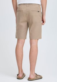 Beige katoenen shorts met elastische tailleband, twee achterzakken en rechte snit die boven de knie eindigt, gecombineerd met brown sandalen.