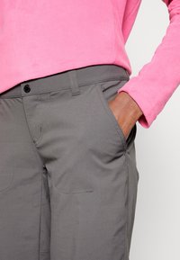 Pantalones grises con una textura suave, que cuentan con bolsillos laterales, un cierre de botón y costuras en contraste, combinados con una parte superior de forro polar rosa.