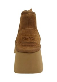 Stivale alla caviglia in suede marrone con suola platform, caratterizzato da un'etichetta posteriore impressa con "KEYS" e una tomaia testurizzata per aderenza e supporto.