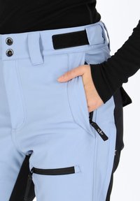Light blue pants featuring black accents, button closure, adjustable waistband with Velcro, and zippered pockets for additional storage.