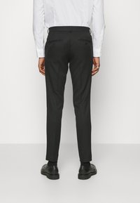 Fekete, sima anyagból készült, testre szabott nadrág, slim fit fazonnal és két hátsó zsebbel. Fekete cipővel és fehér inggel párosítva.