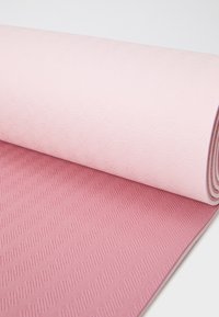Tapis de yoga dans des tons de rose et de rose clair, présentant une surface florale texturée d'un côté et une poignée à motifs de l'autre.