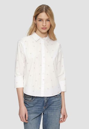 Witte overhemd met roze hartpatronen, lange mouwen en een kraaghalslijn. Gestyled met blauwe spijkerbroek.
