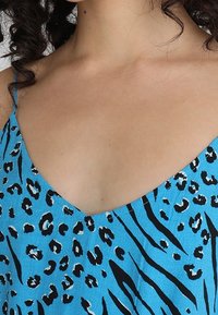 Blå ärmlös topp med leopard- och zebramönster, V-ringning och tunna band, tillverkad av ett lätt tyg.