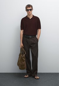 Polo a maniche corte marrone, pantaloni larghi marroni, cintura nera, ciabatte e borsa a tracolla marrone. Il modello indossa occhiali da sole scuri.