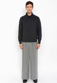 Donkergrijze gebreide trui met een kraag en knoopdetail, gecombineerd met lichtgrijze wijde broek met krijtstreep. Soepele textuur, casual pasvorm.