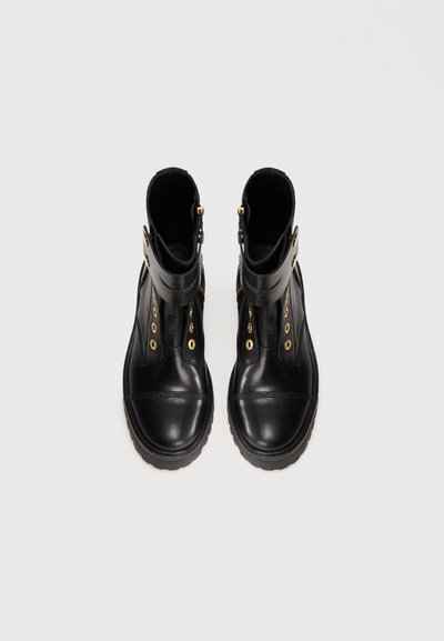 Black leather ankle boots with gold hardware, featuring a rounded toe, side zipper, and decorative lacing on the front.