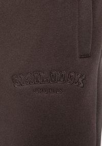Dunkelbraune Sweatpants aus weichem Stoff, mit einem gestickten Logo "SMILODOX ORIGINALS" auf der linken Seite.
