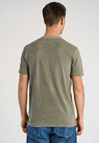 T-shirt a maniche corte, verde oliva, realizzato in tessuto morbido, con scollatura a girocollo e una texture liscia, mostrato dal retro.