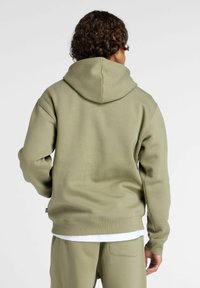 Olijfgroene hoodie, gemaakt van zacht materiaal. Heeft een ontspannen pasvorm, ribgebreide manchetten en een buidelzak.