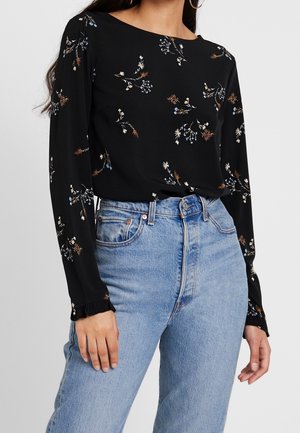 Blouse noire à manches longues avec petits imprimés floraux, associée à un jean bleu clair taille haute sur une femme.